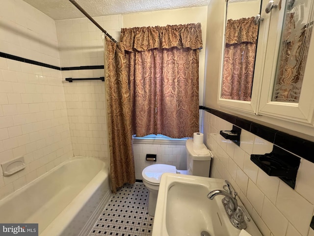 full bathroom with sink, a textured ceiling, tile walls, toilet, and shower / bath combo with shower curtain