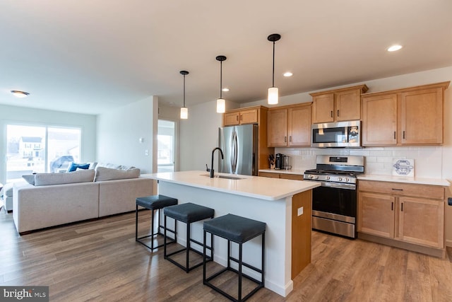 kitchen featuring backsplash, hardwood / wood-style floors, hanging light fixtures, a kitchen island with sink, and stainless steel appliances