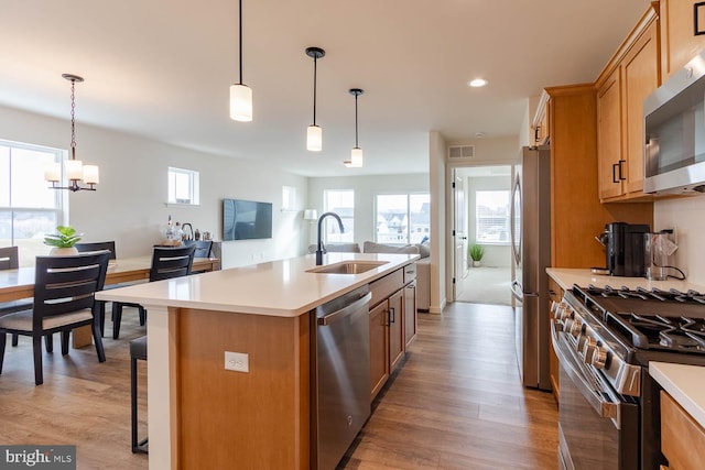 kitchen featuring decorative light fixtures, sink, appliances with stainless steel finishes, and a center island with sink