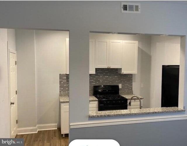 kitchen with black gas range, white cabinets, decorative backsplash, and light stone counters