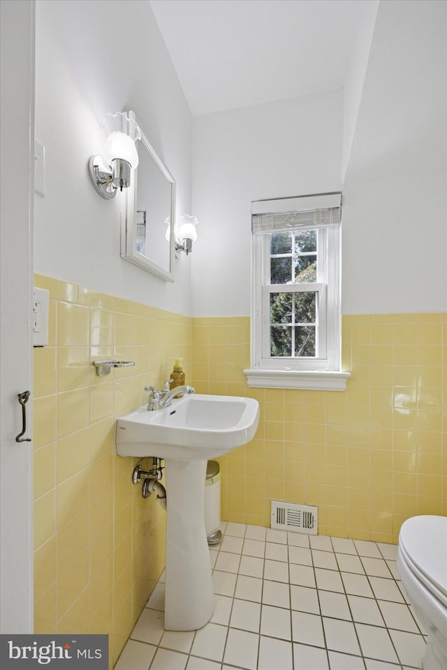 half bath with tile patterned flooring, visible vents, tile walls, and a wainscoted wall