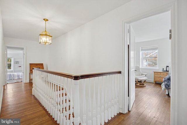 hall featuring baseboards, wood-type flooring, an inviting chandelier, and an upstairs landing