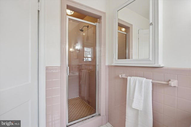 bathroom featuring a wainscoted wall, tile walls, and a stall shower