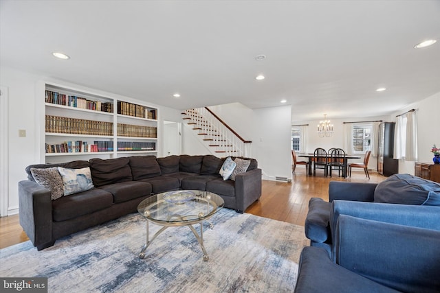 living room with built in shelves, a notable chandelier, hardwood / wood-style floors, recessed lighting, and stairway