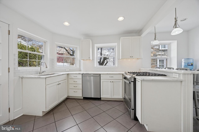 kitchen featuring a sink, white cabinetry, appliances with stainless steel finishes, a peninsula, and decorative backsplash