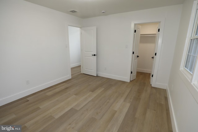 unfurnished bedroom with light hardwood / wood-style floors, a spacious closet, and a closet