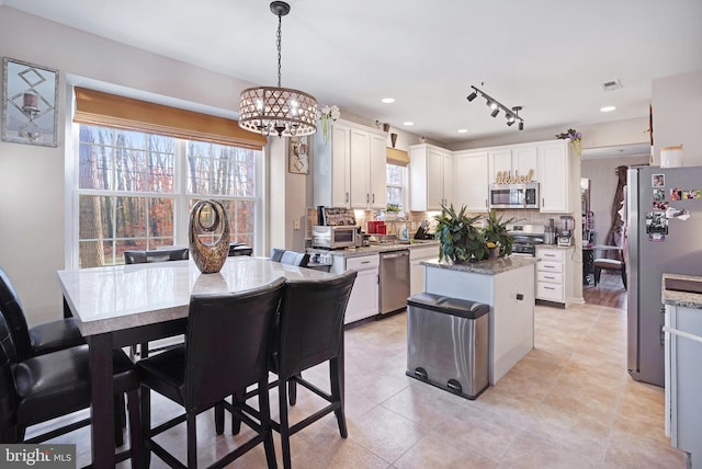 kitchen featuring light stone counters, decorative light fixtures, a center island, appliances with stainless steel finishes, and white cabinets