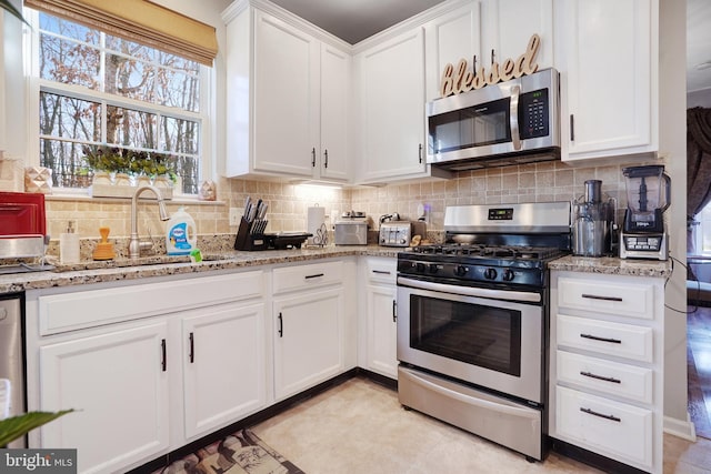 kitchen with sink, backsplash, stainless steel appliances, light stone countertops, and white cabinets