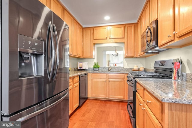 kitchen with light stone counters, stainless steel appliances, sink, and light hardwood / wood-style flooring