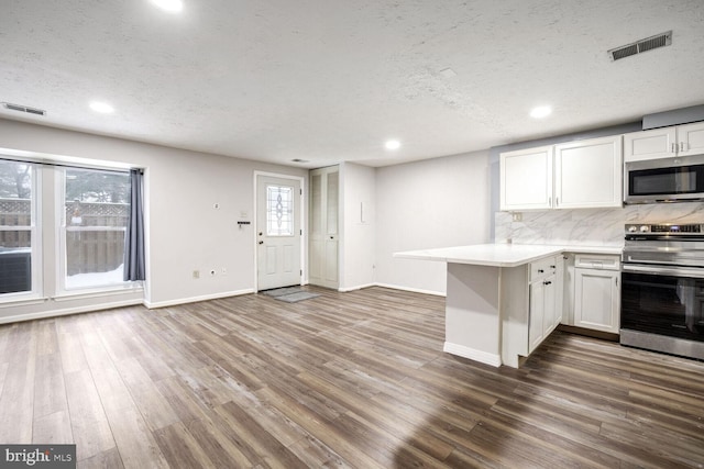 kitchen featuring kitchen peninsula, white cabinets, a textured ceiling, decorative backsplash, and stainless steel appliances