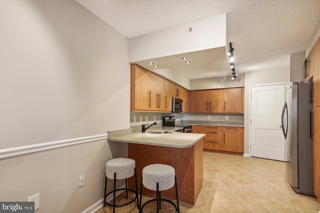 kitchen with sink, a textured ceiling, a kitchen breakfast bar, kitchen peninsula, and stainless steel appliances