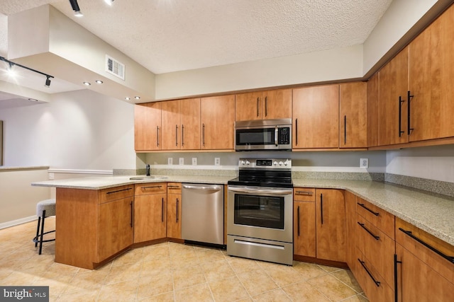 kitchen with sink, a breakfast bar area, a textured ceiling, kitchen peninsula, and stainless steel appliances