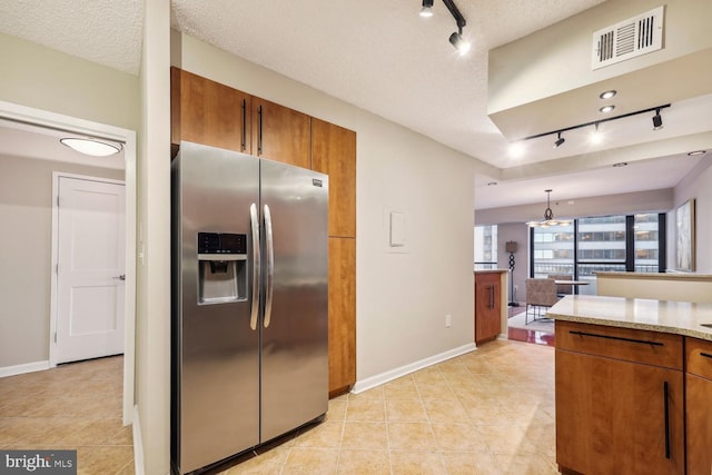 kitchen with decorative light fixtures, rail lighting, stainless steel fridge, light stone counters, and a textured ceiling