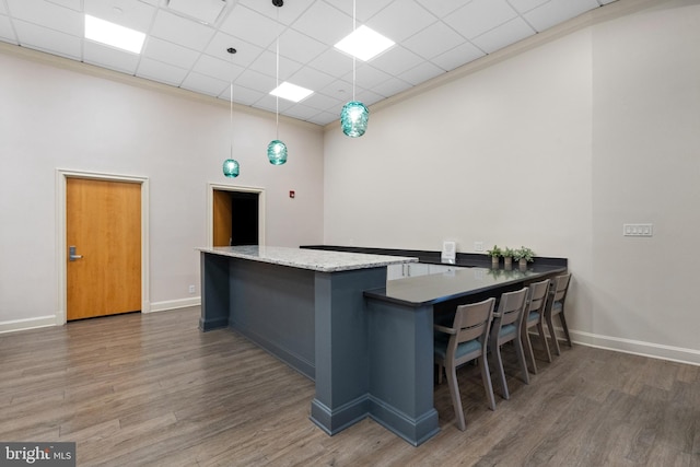 kitchen featuring a breakfast bar area, a paneled ceiling, decorative light fixtures, dark hardwood / wood-style flooring, and kitchen peninsula