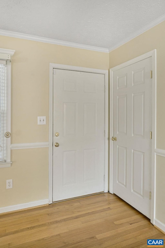 foyer entrance with a textured ceiling, ornamental molding, and light hardwood / wood-style flooring