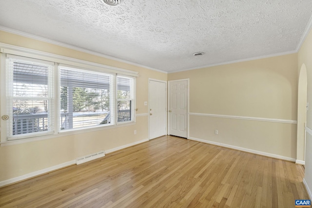 empty room with a textured ceiling, light wood-type flooring, and crown molding