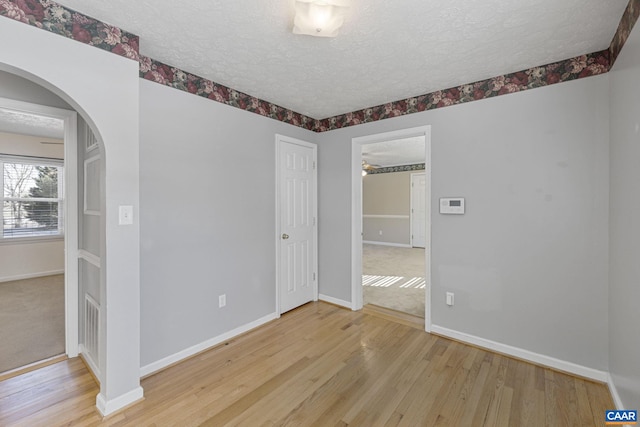 empty room with a textured ceiling, ceiling fan, and light hardwood / wood-style flooring