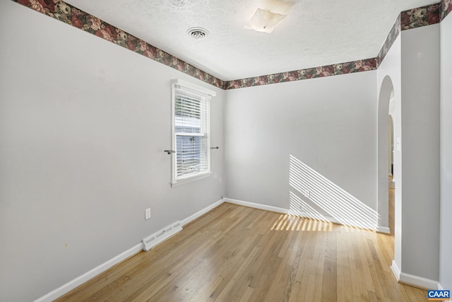 empty room with a textured ceiling and light hardwood / wood-style floors