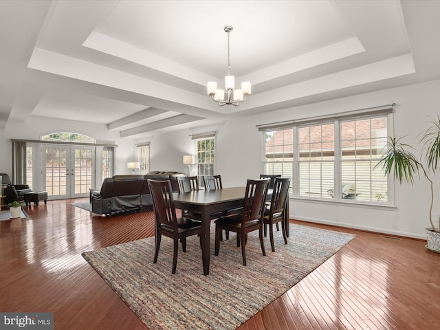 dining area featuring plenty of natural light, a raised ceiling, wood finished floors, french doors, and a notable chandelier