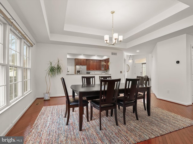 dining space with dark wood-style flooring, a raised ceiling, and a notable chandelier