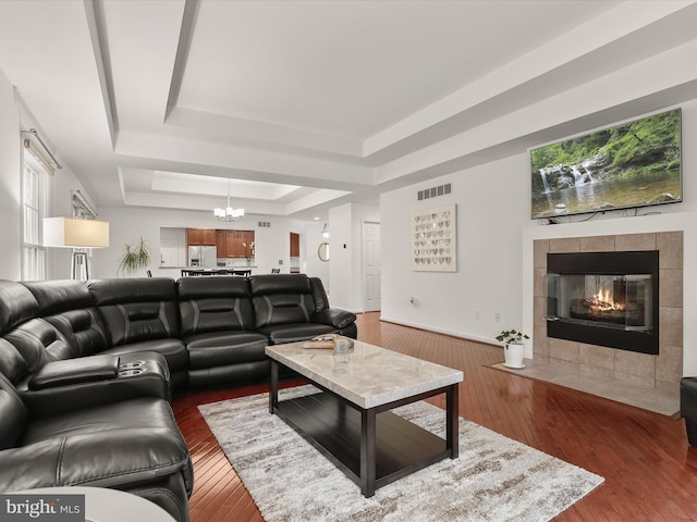 living area with dark wood-style floors, a raised ceiling, visible vents, and a tiled fireplace