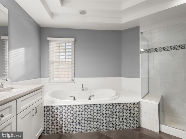 full bathroom with a tray ceiling, a garden tub, vanity, and a shower stall