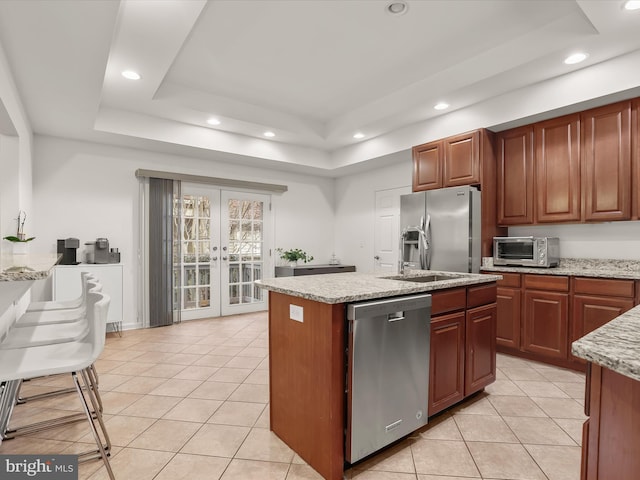 kitchen with stainless steel appliances, french doors, light stone countertops, a raised ceiling, and a center island with sink