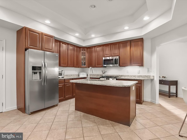 kitchen featuring light tile patterned floors, appliances with stainless steel finishes, a raised ceiling, and light stone counters