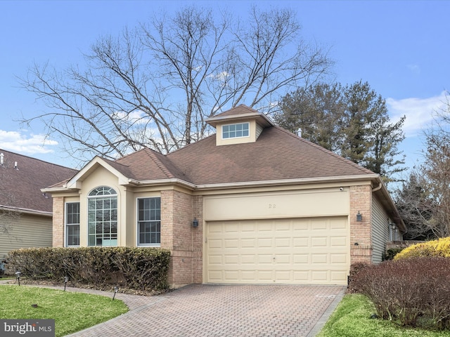 view of front facade with a garage, roof with shingles, brick siding, and decorative driveway