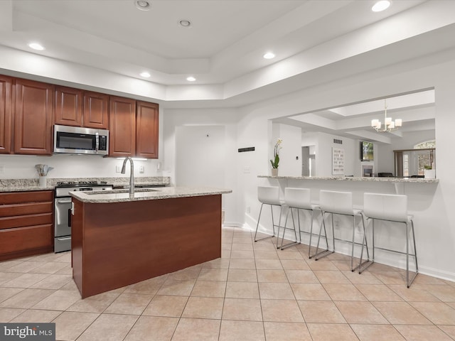 kitchen featuring a breakfast bar, hanging light fixtures, light stone countertops, a tray ceiling, and stainless steel appliances