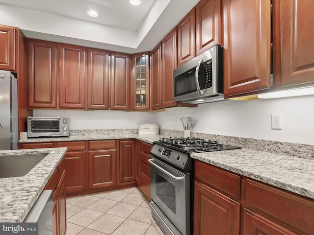 kitchen with stainless steel appliances, glass insert cabinets, and light stone countertops