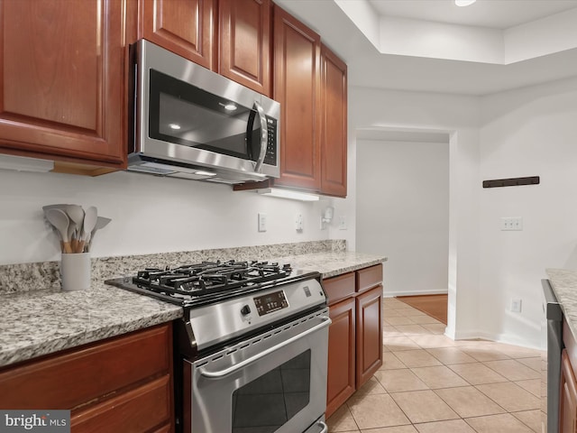 kitchen featuring light tile patterned floors, light stone counters, stainless steel appliances, baseboards, and a tray ceiling