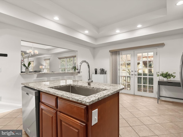 kitchen with a sink, light stone countertops, dishwasher, a tray ceiling, and a center island with sink