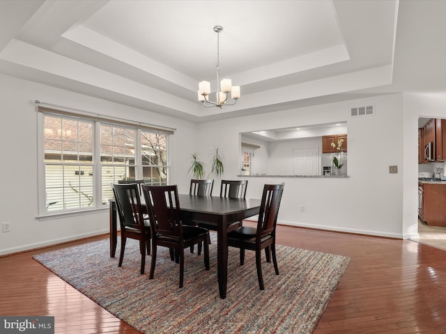 dining room featuring dark wood-style flooring, visible vents, a raised ceiling, and a notable chandelier