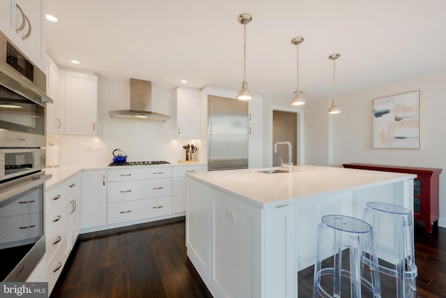 kitchen with a center island with sink, appliances with stainless steel finishes, decorative backsplash, decorative light fixtures, and wall chimney exhaust hood