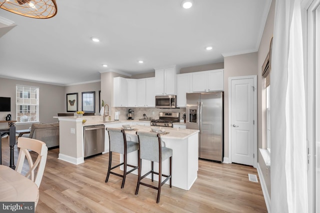 kitchen with kitchen peninsula, light wood-type flooring, white cabinets, appliances with stainless steel finishes, and a kitchen breakfast bar