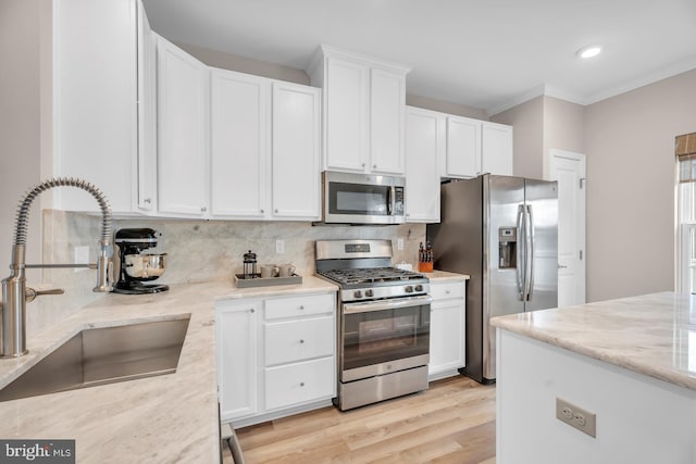 kitchen featuring appliances with stainless steel finishes, light stone counters, white cabinets, light hardwood / wood-style flooring, and sink