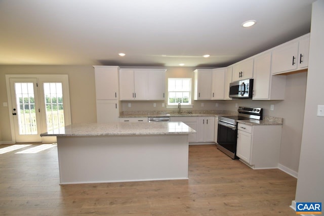 kitchen with stainless steel appliances, white cabinets, a center island, and light stone counters