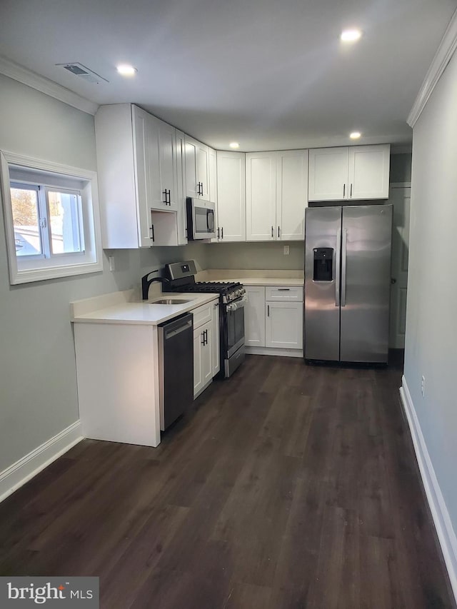 kitchen with dark wood-type flooring, white cabinets, appliances with stainless steel finishes, and crown molding