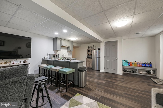 kitchen featuring stainless steel fridge, gray cabinets, a breakfast bar, dark hardwood / wood-style floors, and a drop ceiling