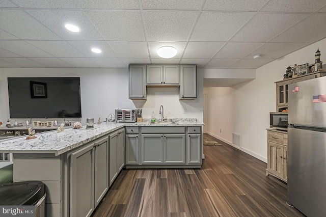 kitchen with appliances with stainless steel finishes, sink, gray cabinetry, dark hardwood / wood-style flooring, and kitchen peninsula