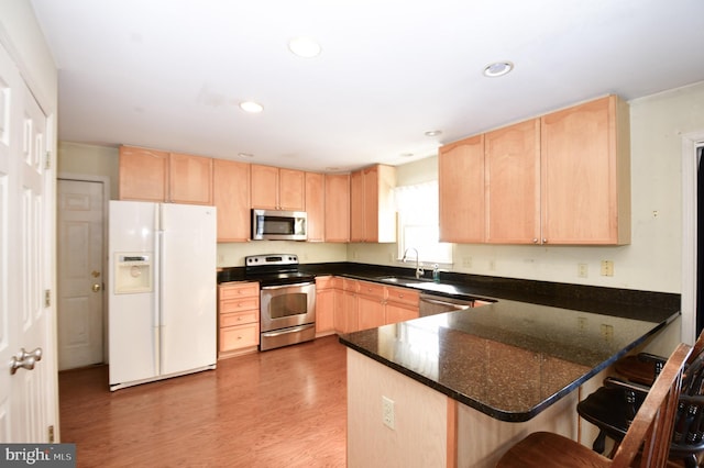 kitchen with a breakfast bar, stainless steel appliances, light brown cabinetry, and kitchen peninsula