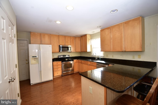 kitchen with stainless steel appliances, sink, kitchen peninsula, dark stone counters, and a breakfast bar