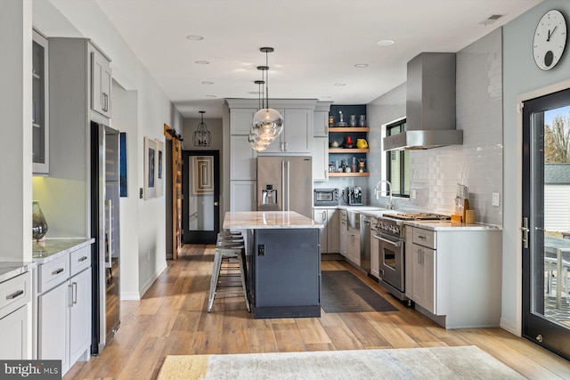 kitchen featuring high quality appliances, wall chimney exhaust hood, light stone counters, a center island, and decorative backsplash