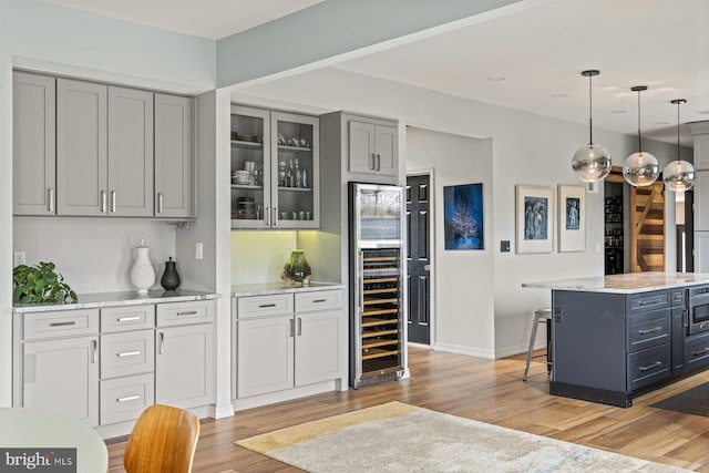 kitchen with gray cabinets, hanging light fixtures, light stone countertops, and beverage cooler