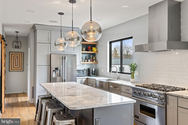 kitchen featuring a center island, premium appliances, wall chimney range hood, a breakfast bar, and light stone counters