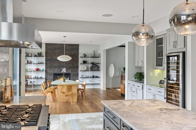 kitchen with hanging light fixtures, wine cooler, extractor fan, and light stone counters