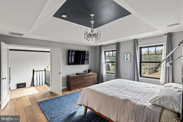 bedroom featuring wood-type flooring, a notable chandelier, and a raised ceiling