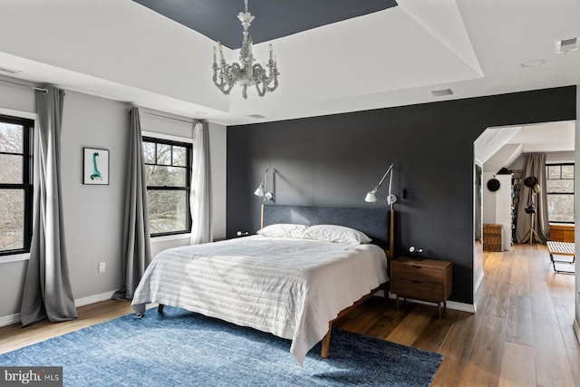 bedroom featuring hardwood / wood-style flooring, a tray ceiling, and an inviting chandelier