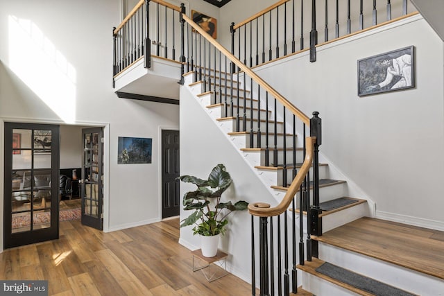 staircase with french doors, wood-type flooring, and a towering ceiling